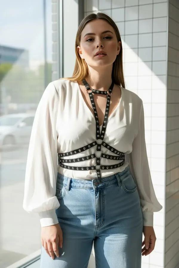 black faux leather chest harness with silver rivets and central O-ring worn over white oversized shirt
