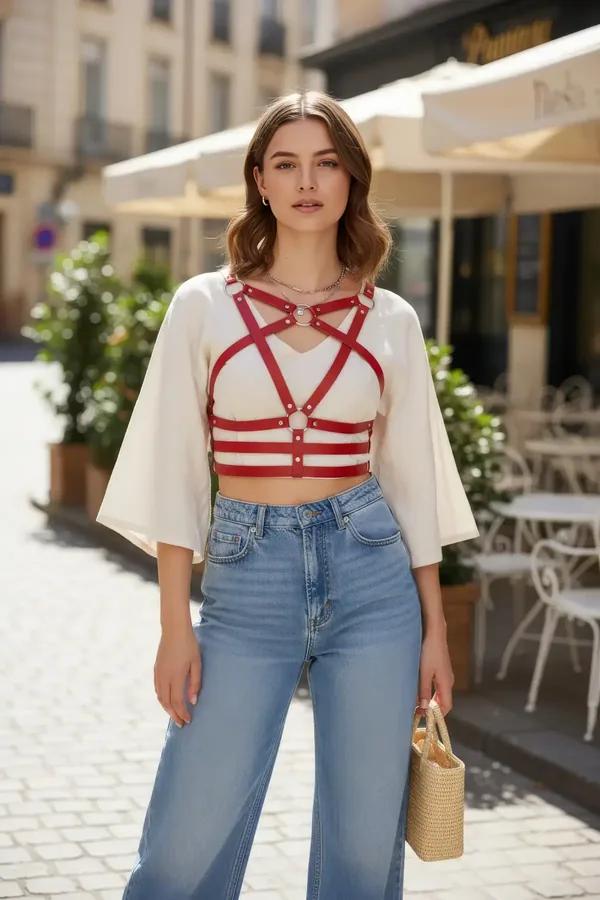 red faux leather caged chest harness with silver O-rings worn over white crop top, geometric star-cross strap design