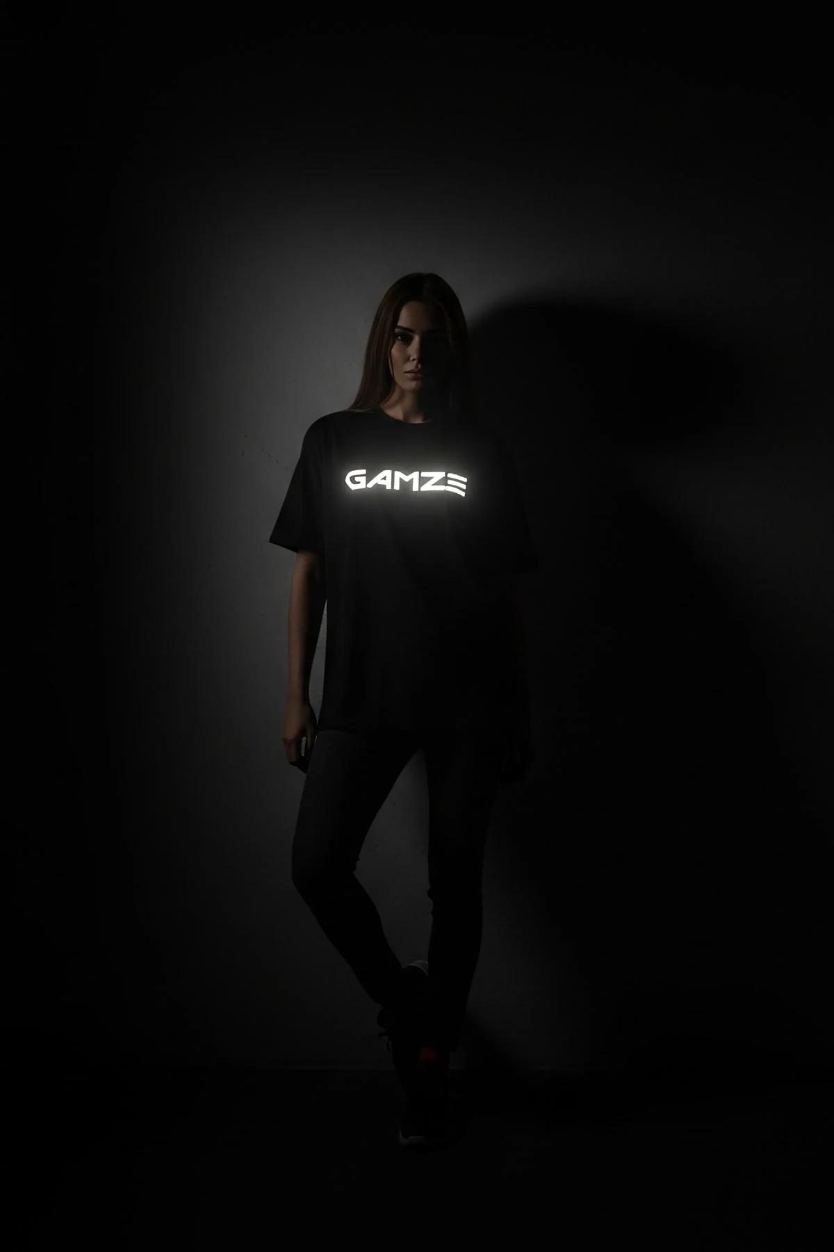 black reflective graphic t-shirt with bold custom text glowing bright white on chest in low-light studio shot