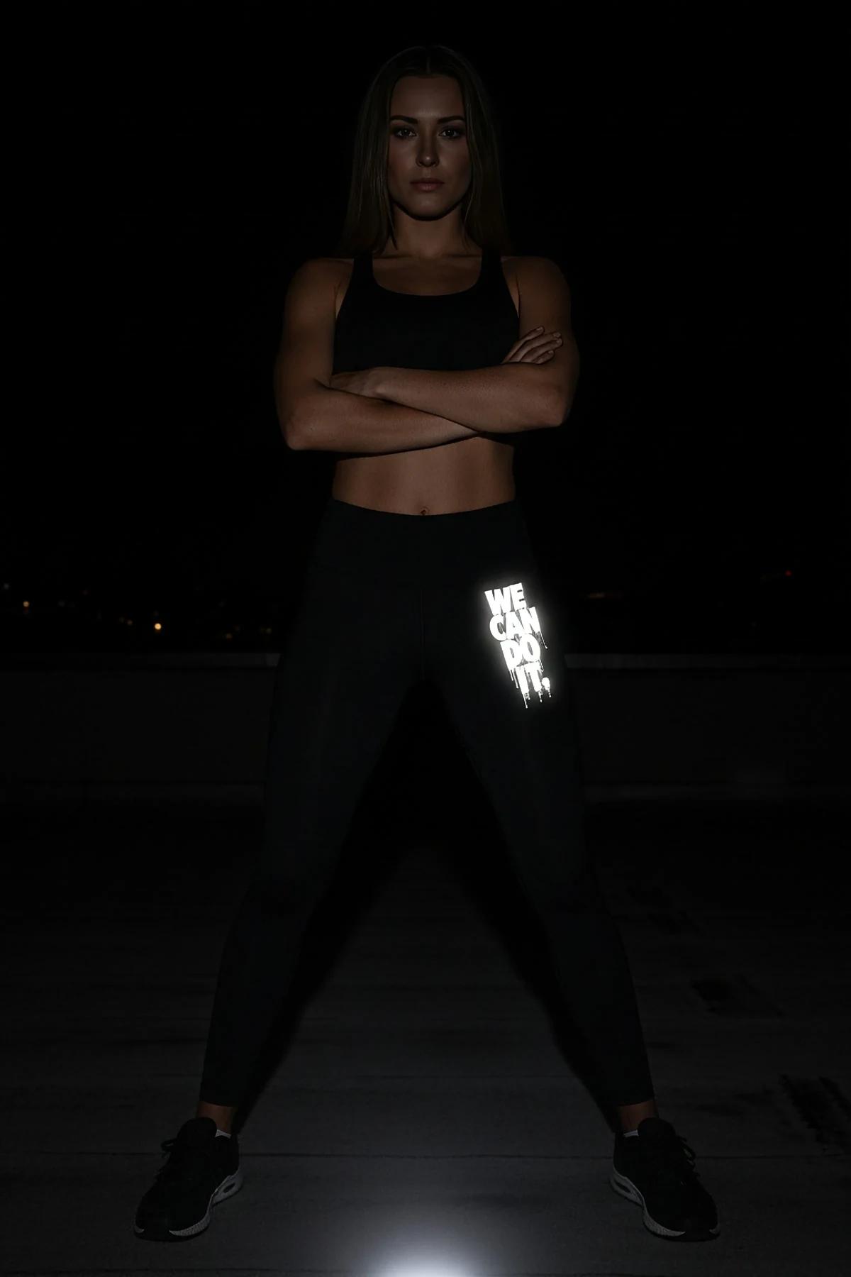 black high-waist leggings with white retroreflective We Can Do It graffiti-drip print on left thigh photographed at night