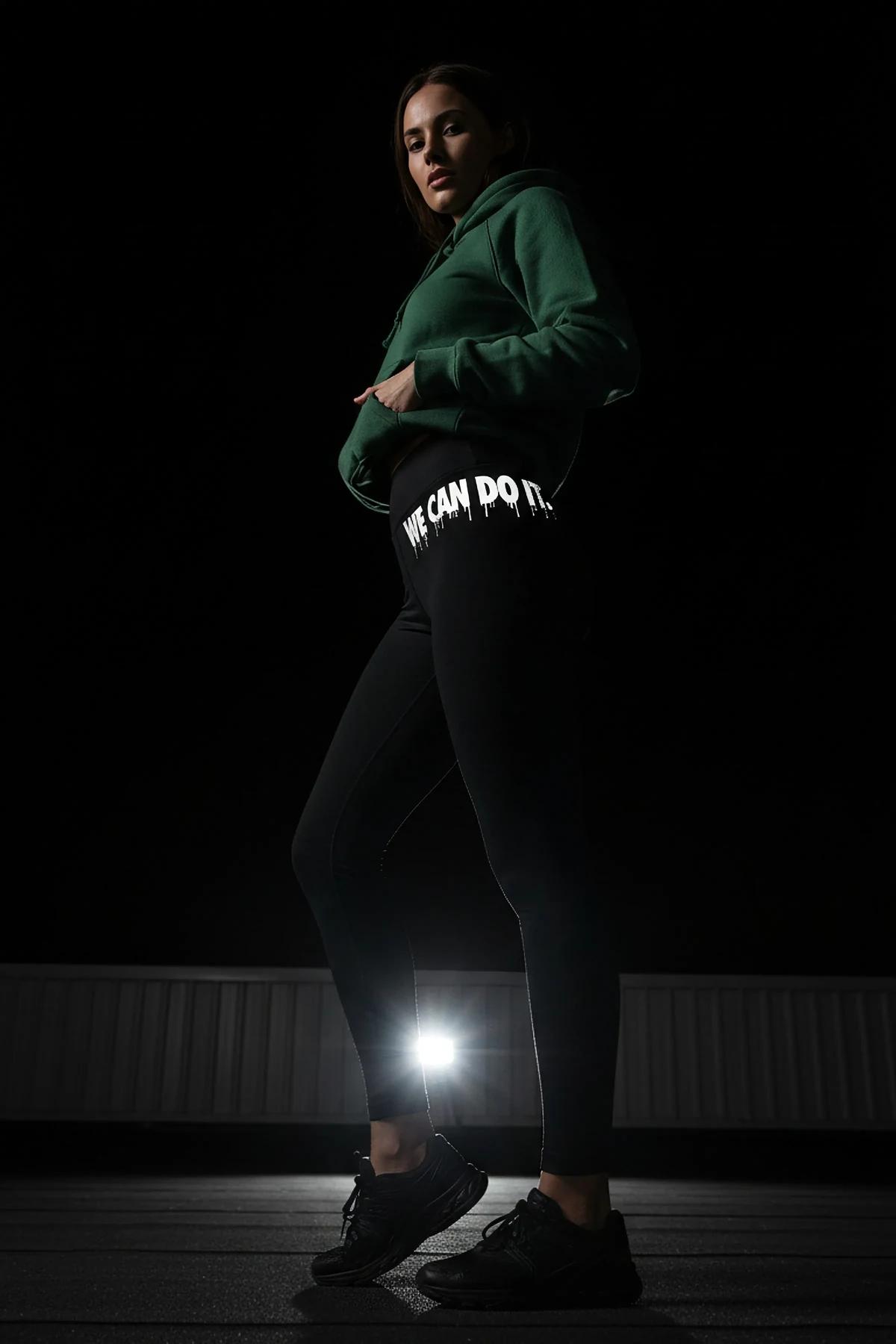 black high-waist leggings with white retroreflective We Can Do It graffiti-drip print on left thigh photographed at night