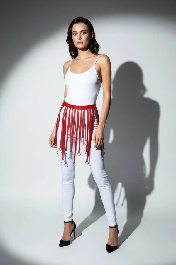 red faux leather waist harness with silver O-ring fringe straps worn over white leggings and bodysuit