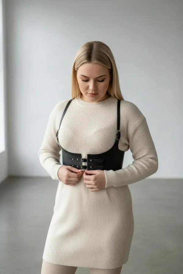 black faux leather underbust harness with wide straps and silver buckles worn over cream ribbed sweater