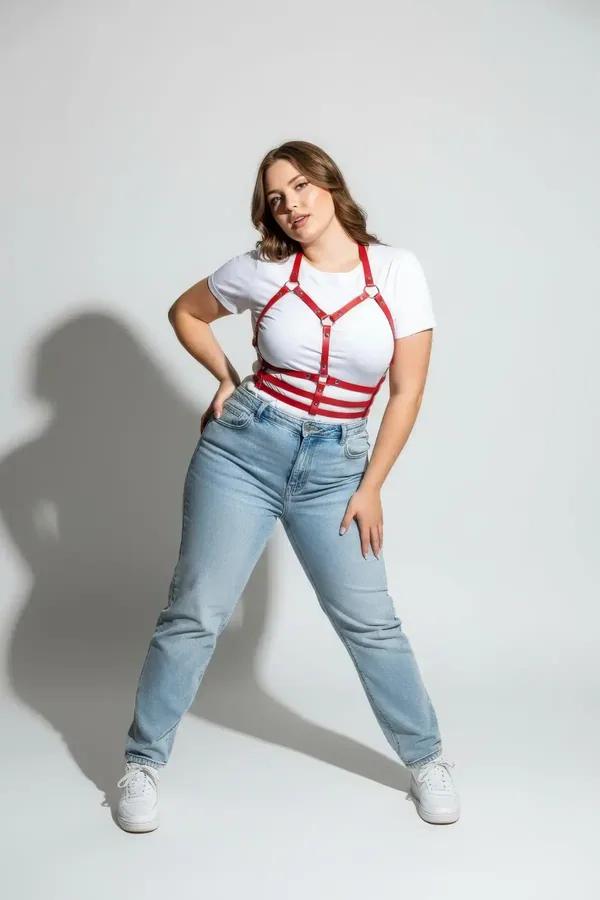 red faux leather strappy chest and waist harness with silver O-rings worn over white t-shirt