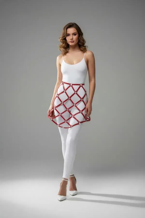 Red faux leather lattice skirt harness with silver stud intersections worn over white bodysuit and leggings