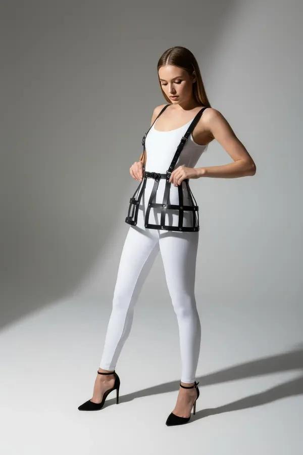 black faux leather cage skirt harness with shoulder straps and riveted geometric grid panels worn over white bodysuit