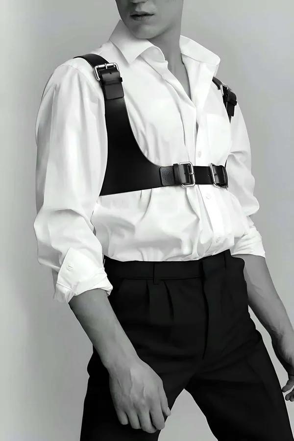 Black faux leather men's chest harness with wide shoulder straps and dual silver rectangular buckles worn over a white shirt