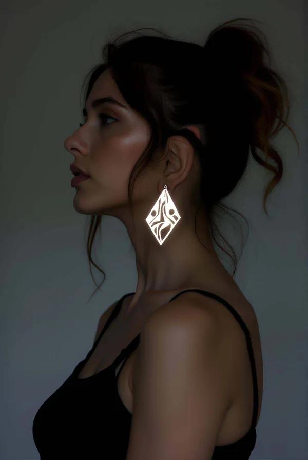 Gümüş renkli elmas formlu reflektörlü lazer kesim geometrik küpe, tribal motifli metalik yüzey, model kulağında