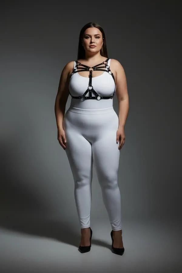 black faux leather strappy chest harness with silver O-rings worn over white bodysuit plus size model