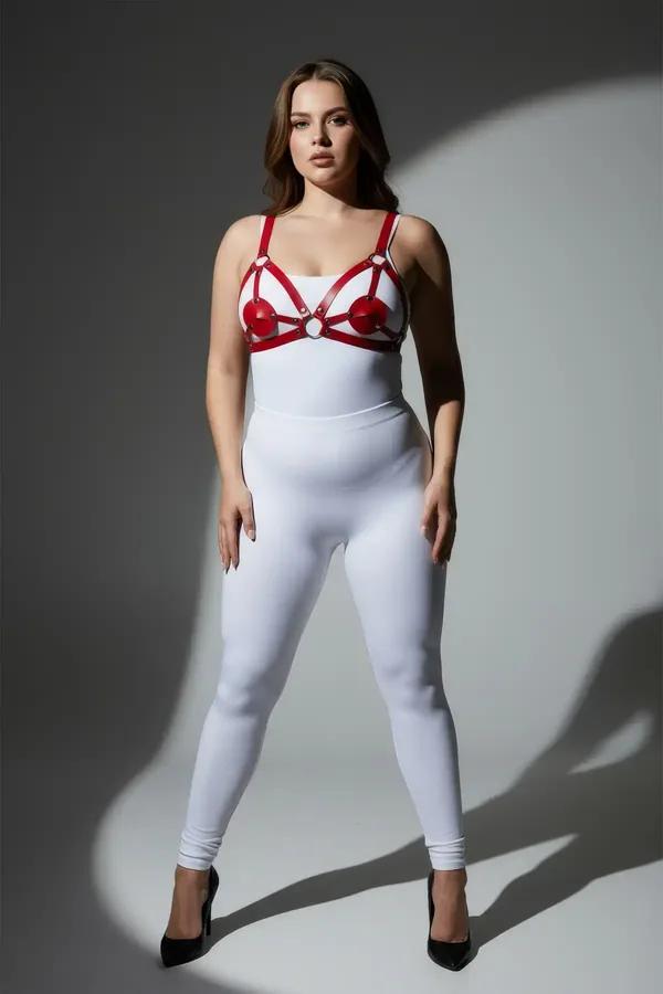 Red strappy chest harness with heart-shaped cup panels and silver O-ring on plus-size model over white bodysuit