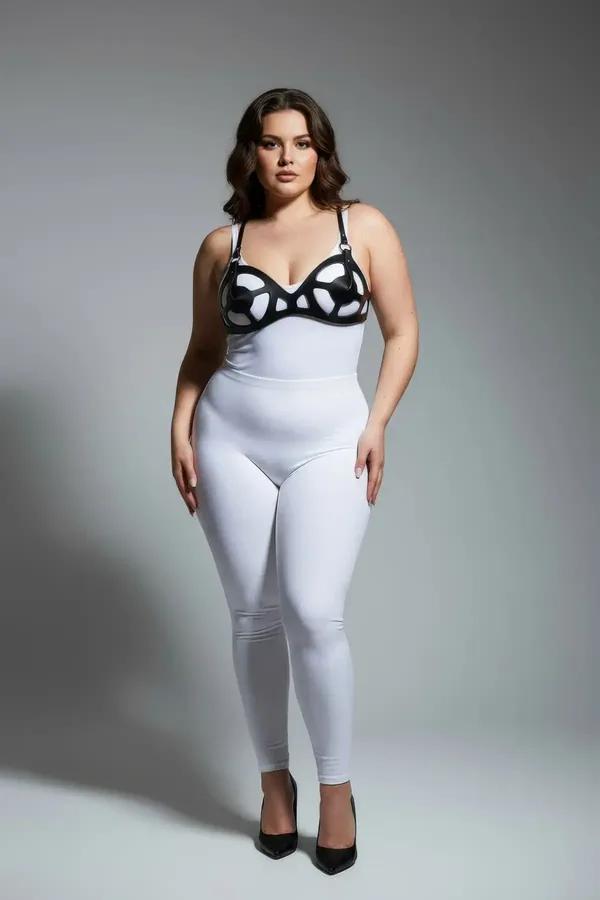 Black faux leather cage bra harness with curved organic cutout panels and silver hardware, worn over white bodysuit