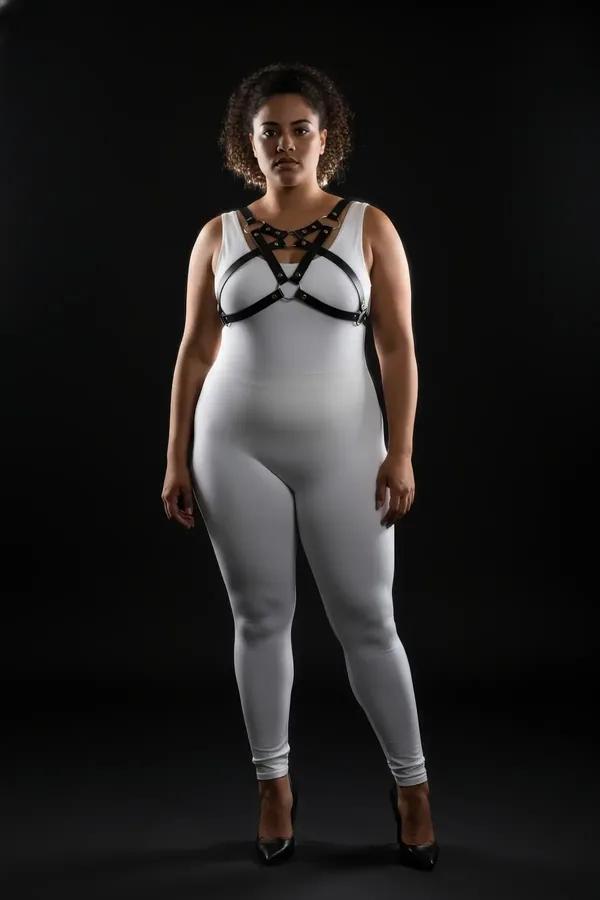 black faux leather chest harness with crossed straps silver studs and central O-ring worn over white outfit