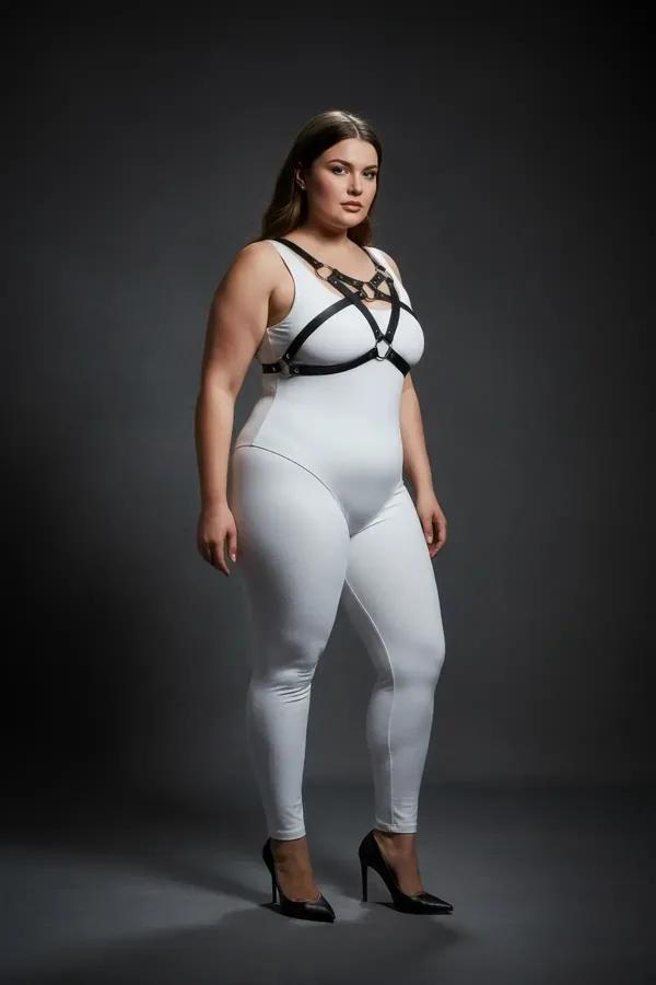 black faux leather chest harness with crossed straps silver studs and central O-ring worn over white outfit