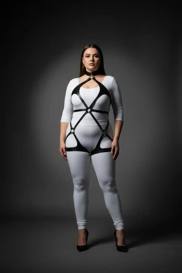 black vegan leather full body harness with neck collar, gold O-ring chest detail, and thigh straps worn over white bodysuit