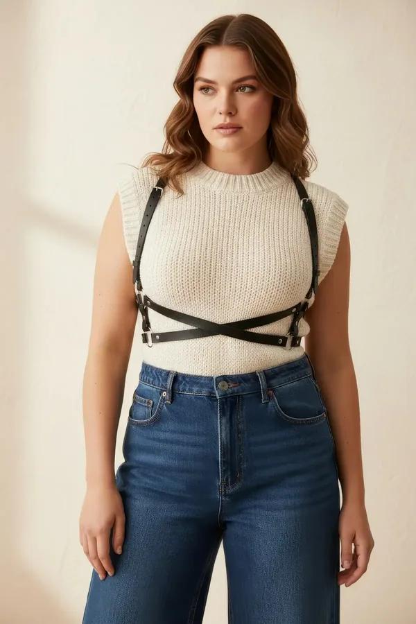 black faux leather chest harness with X-crossover underbust straps and silver buckles worn over cream ribbed sweater