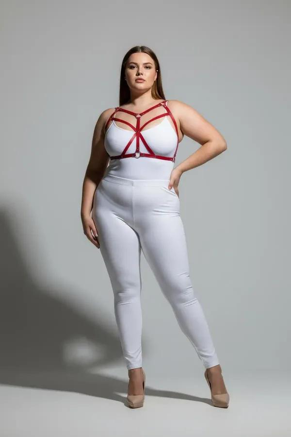 Strappy red faux leather body harness with silver O-ring worn over white bodysuit, plus-size model