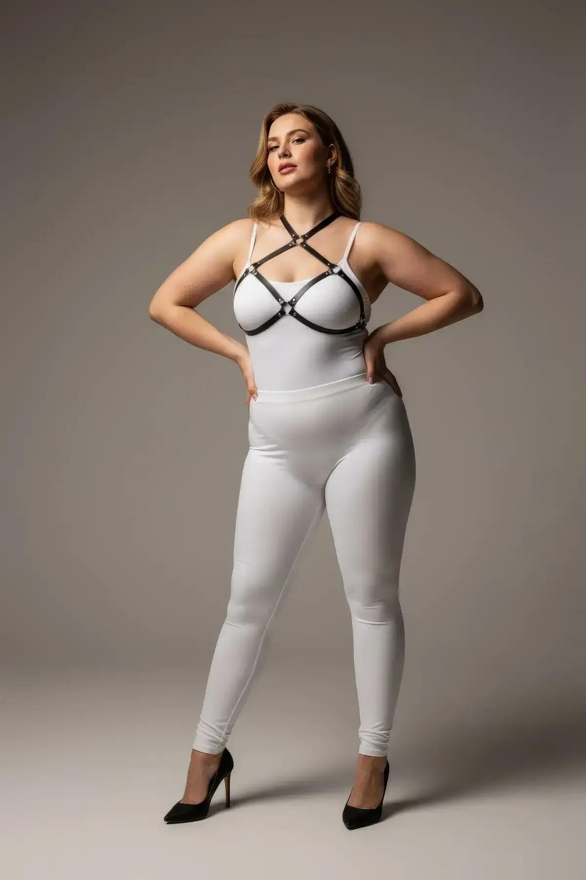 Black faux leather strappy o-ring chest harness with silver connectors worn over white bodysuit, plus-size model
