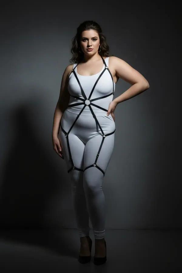 Black faux leather full body harness with gold O-ring chest detail and thigh strap cages worn over white bodysuit