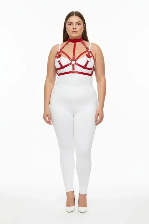 Red faux leather strappy chest harness with three silver O-rings, adjustable cage silhouette worn over white long-sleeve top