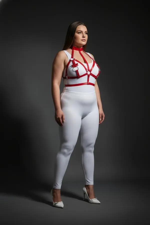 Red faux leather strappy chest harness with three silver O-rings, adjustable cage silhouette worn over white long-sleeve top