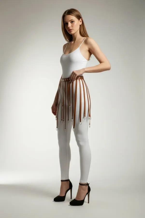 tan faux leather waist harness with multiple draping straps and gold O-ring tips worn over white leggings