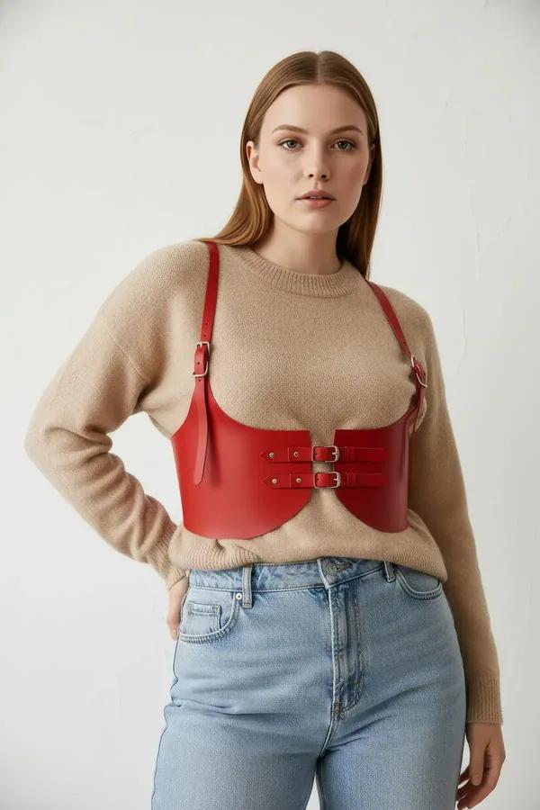 red faux leather underbust waist harness with dual silver buckles worn over cream knit sweater
