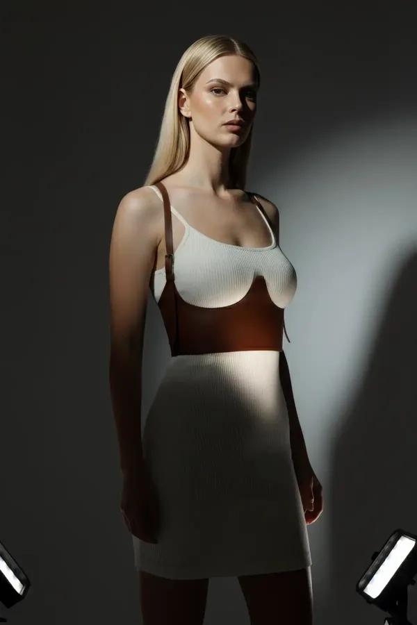 Brown faux leather underbust harness with sculpted bust cups and adjustable gold-buckle shoulder straps worn over white ribbe