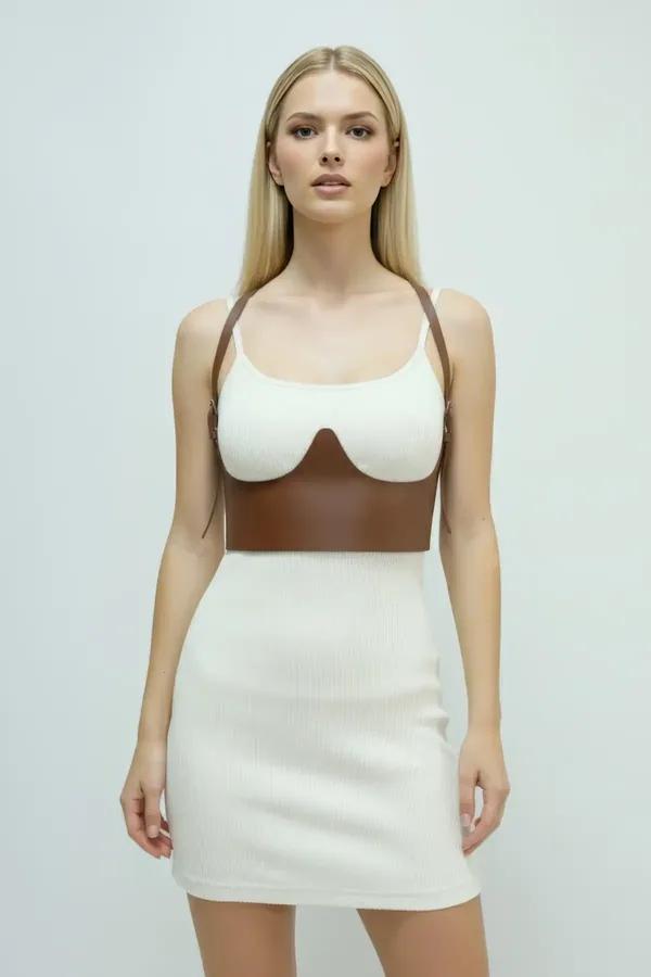 Brown faux leather underbust harness with sculpted bust cups and adjustable gold-buckle shoulder straps worn over white ribbe