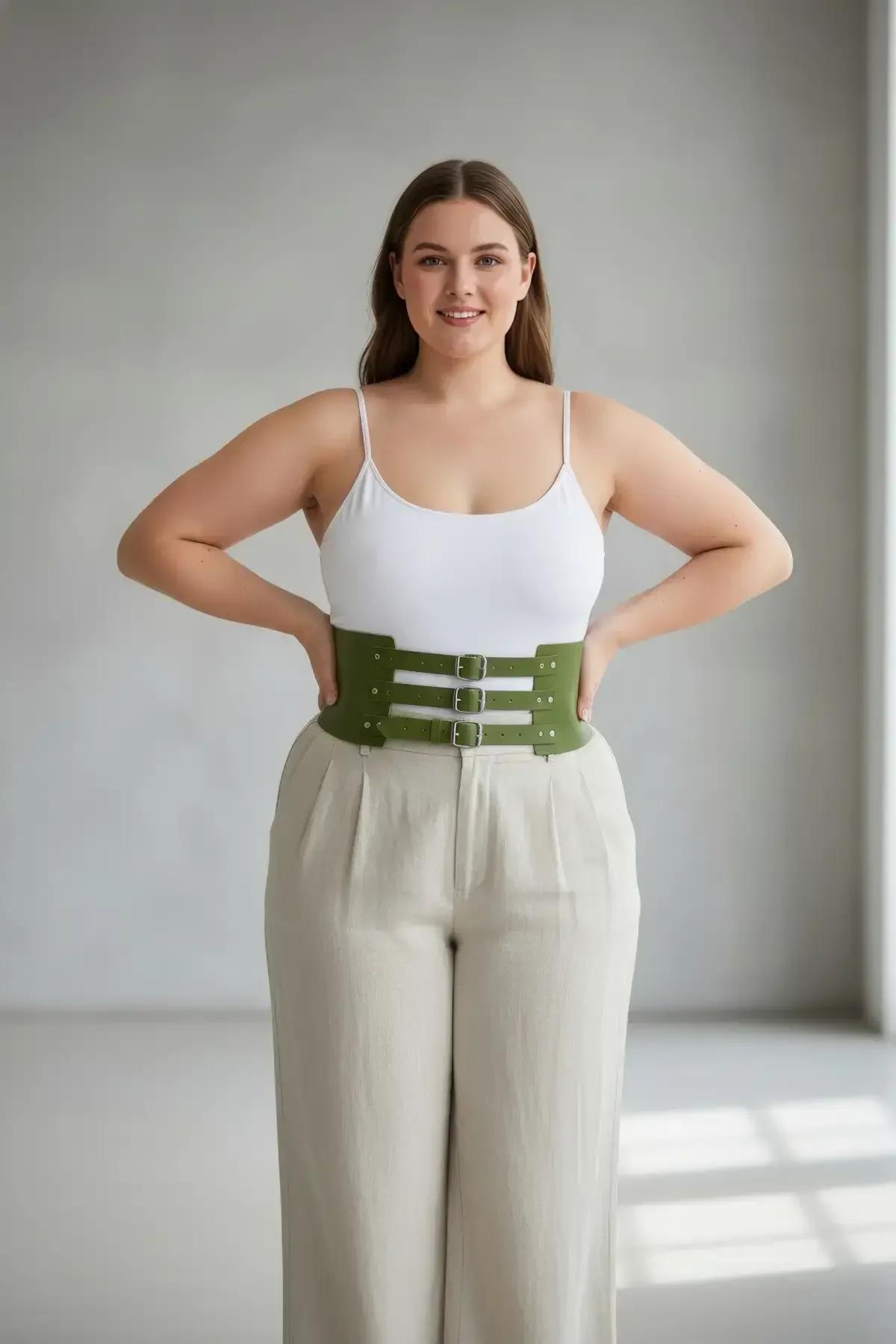 olive green faux leather wide waspie belt with three silver prong buckles worn over white bodysuit and cream trousers