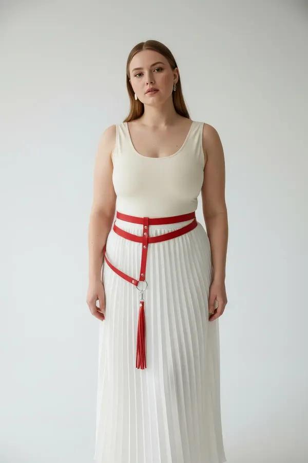 Red faux leather waist harness with silver O-rings and detachable red tassel thigh straps worn over cream trousers