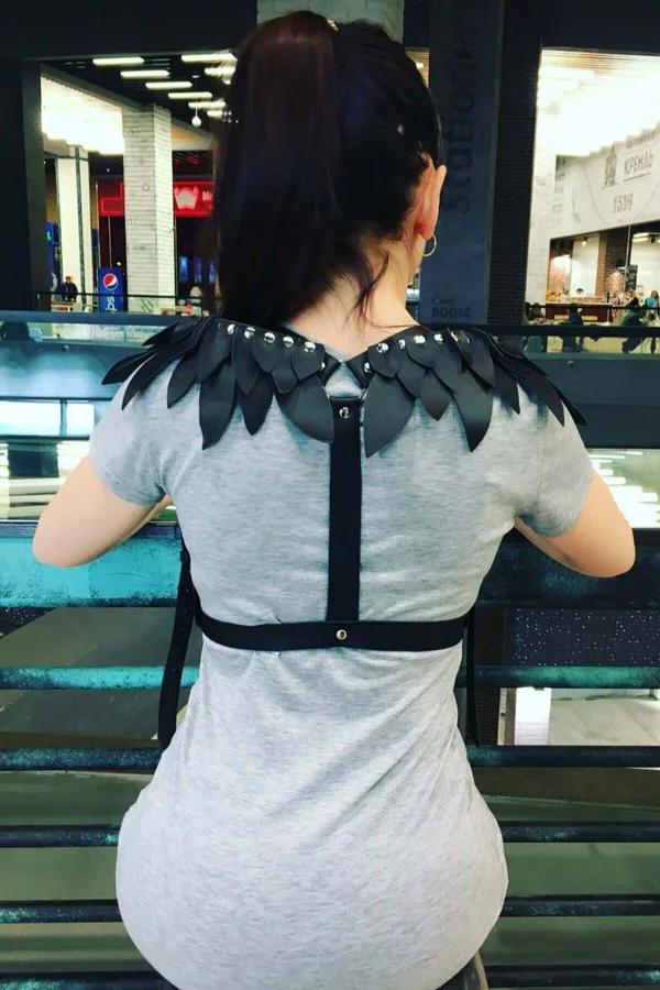 Siyah vegan deri kanatlı omuz harness, gümüş zımba detaylı, gri tişört üstünde arka görünüm