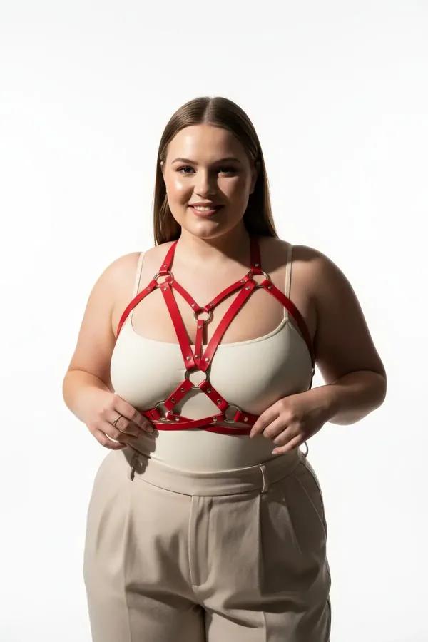 red faux leather caged chest harness with three gold-tone O-rings worn over cream fitted top, symmetrical cage strap design