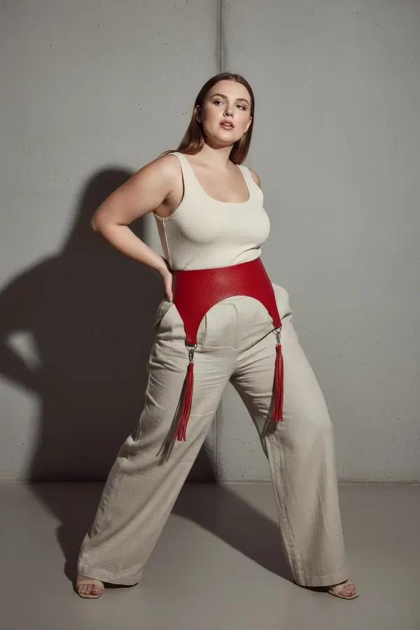 red wide faux leather waist belt harness with matching red tassels and silver hardware worn over white tank and beige skirt