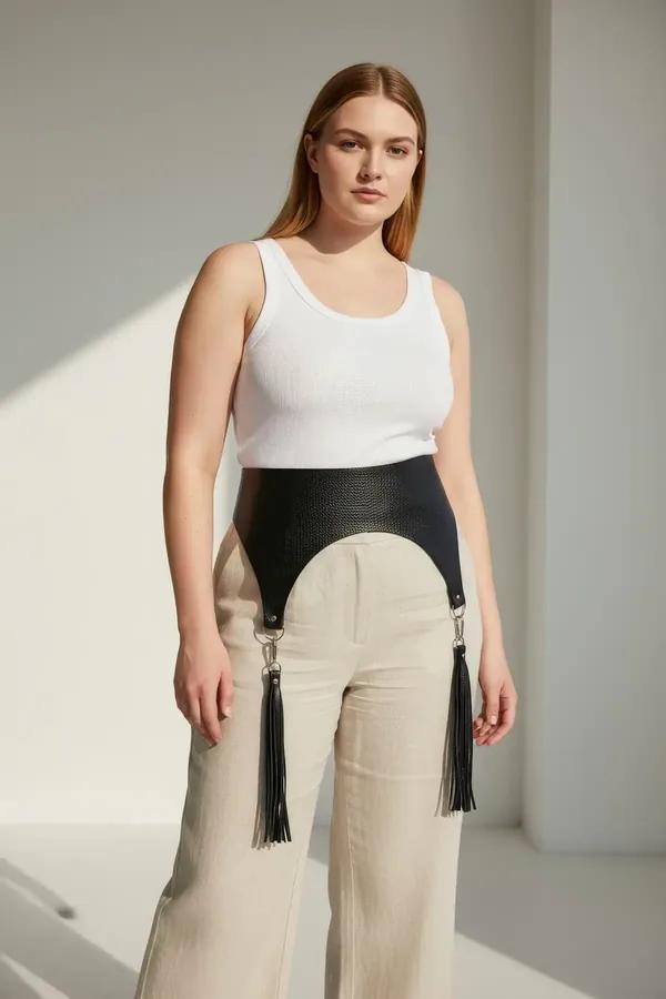 black faux leather wide waist harness with dangling tassels and silver clip hardware worn over cream wide-leg trousers