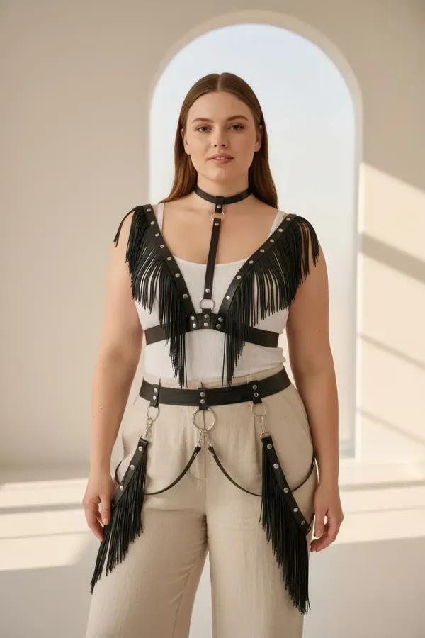black faux leather fringed body harness with silver studs, attached choker, and hip chains worn over cream trousers