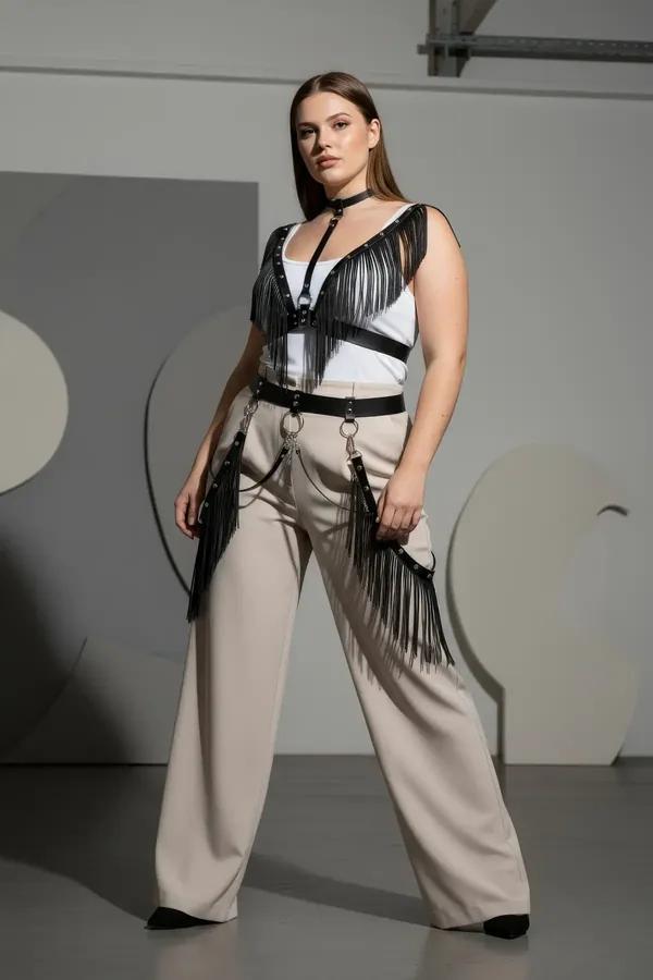 black faux leather fringed body harness with silver studs, attached choker, and hip chains worn over cream trousers
