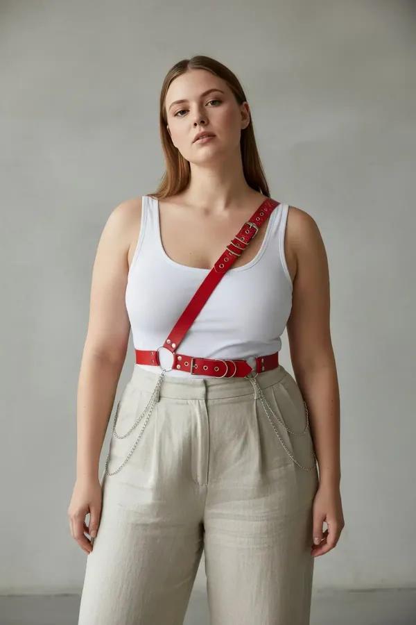 red faux leather single shoulder body harness with silver studs and O-ring worn over white tank top