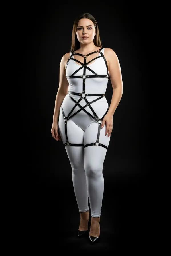 black faux leather full body cage harness with gold O-ring hardware worn over white bodysuit, chest and thigh straps visible