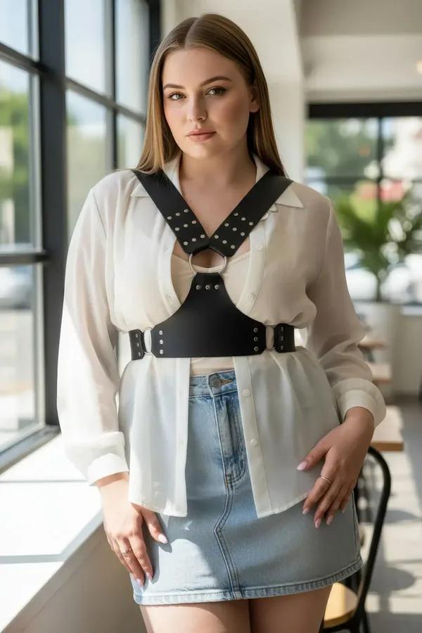 black faux leather chest harness with silver studs and front O-ring worn over cream knit sweater