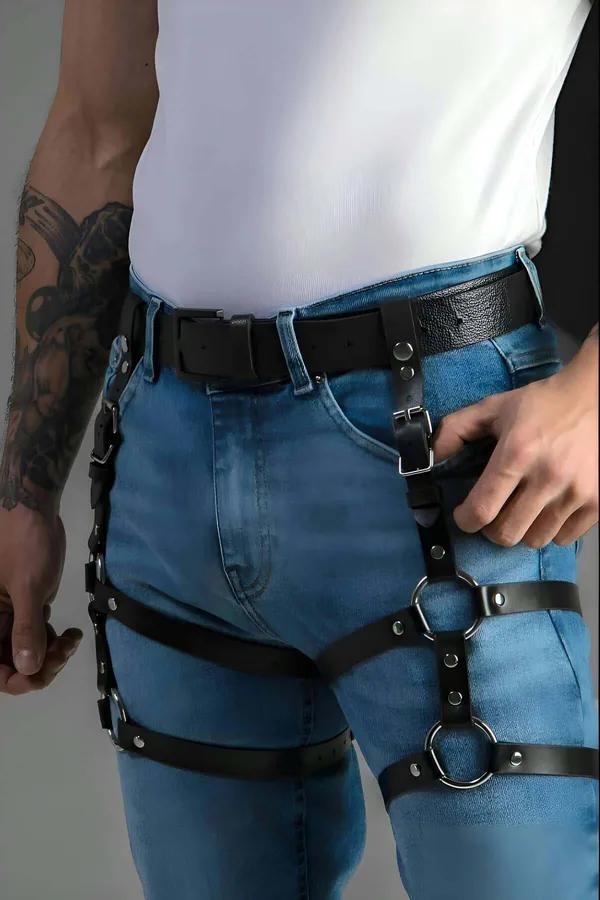 Black faux leather leg harness with silver O-rings worn over blue jeans, waist-to-thigh multi-strap configuration