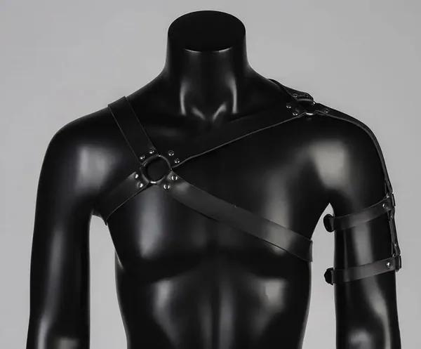 black vegan leather asymmetric chest harness with single shoulder strap, two silver O-rings, rivet studs, and separate upper