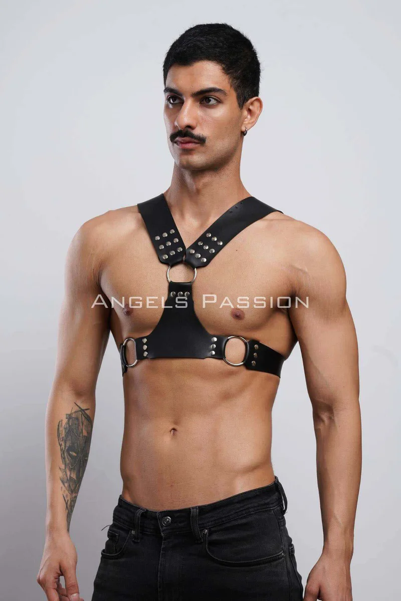 Model wearing black studded chest harness layered over a shirt